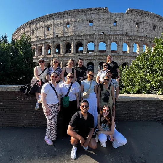 Group of people smiling together in front of the Colosseum in Rome.