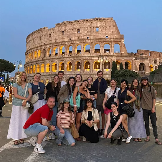 Group of people smiling together in various poses outside the Roman Colosseum in the early evening.