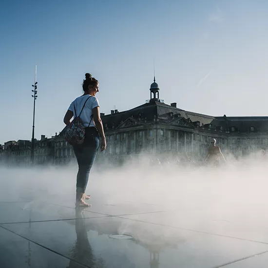 Woman stands barefoot on the Miroir d'eau (Water Mirror), a public art installation in Bordeaux.