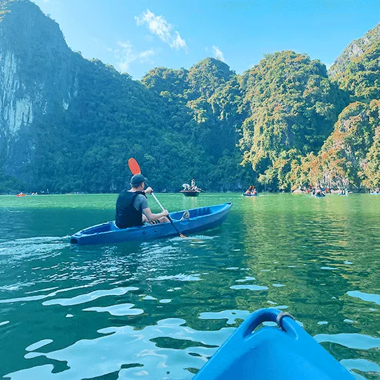 People paddling kayaks in a bay with bright green water in Vietnam.
