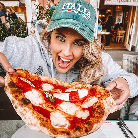 Topdeck traveler about to take a large bite of a Pizza in Venice.
