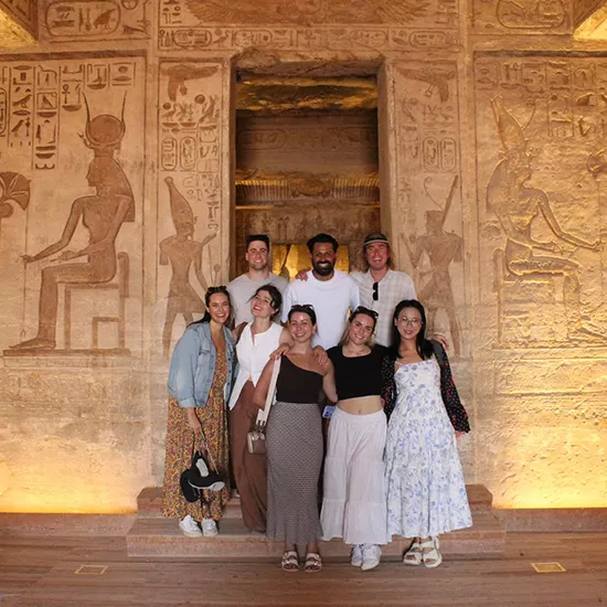 Group of people standing in front of a wall of Egyptian hieroglyphics.